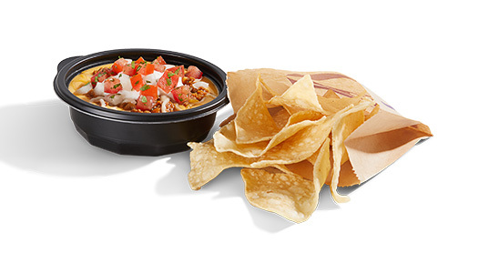 A bag of corn tortilla chips next to a dish of cheese sauce. The sauce is topped with pico de gallo.